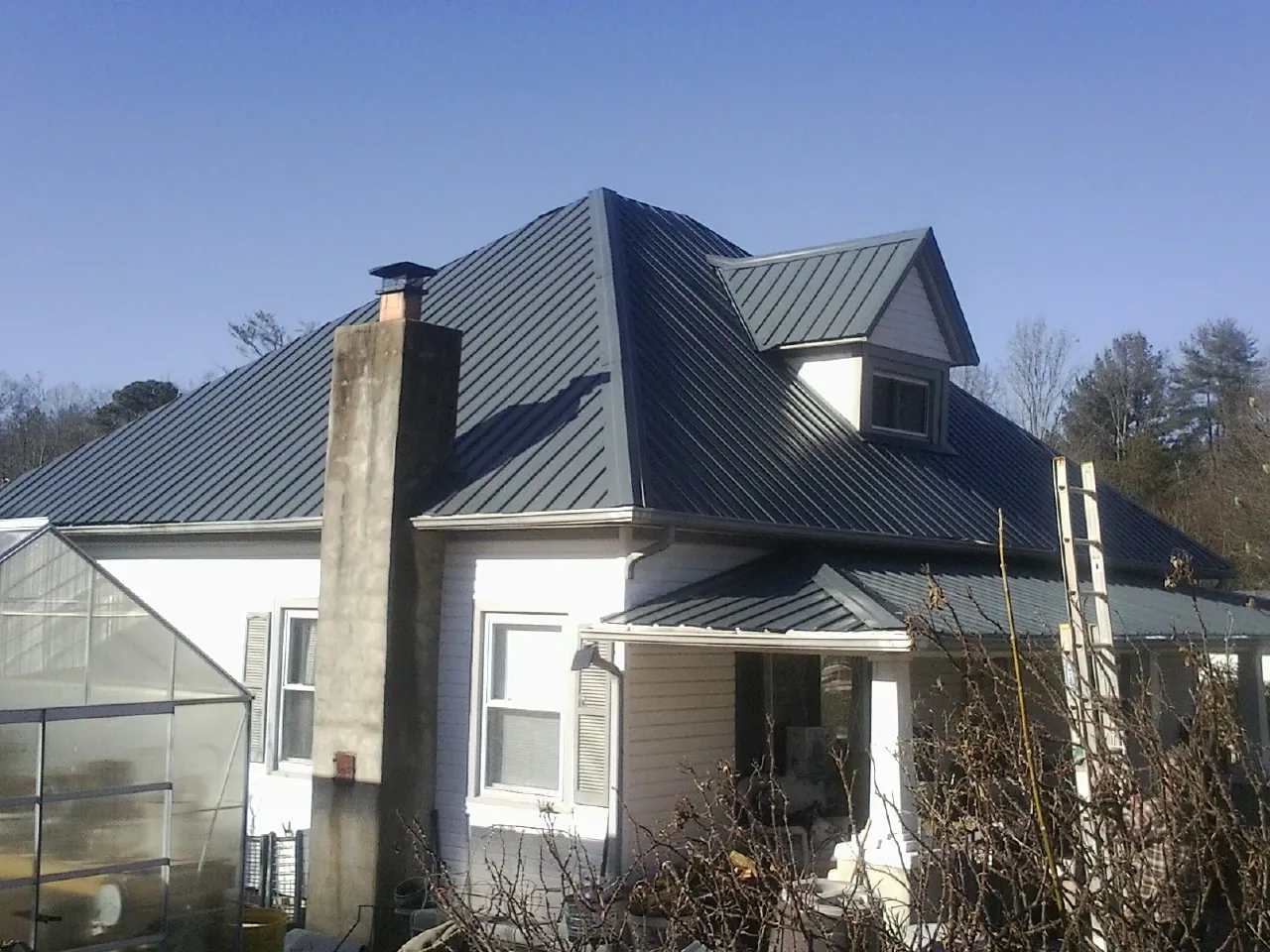 Dark blue standing seam metal roof on a white farmhouse with dormer — Slate & Tile Roof Repair by Roofing Brothers in Culver