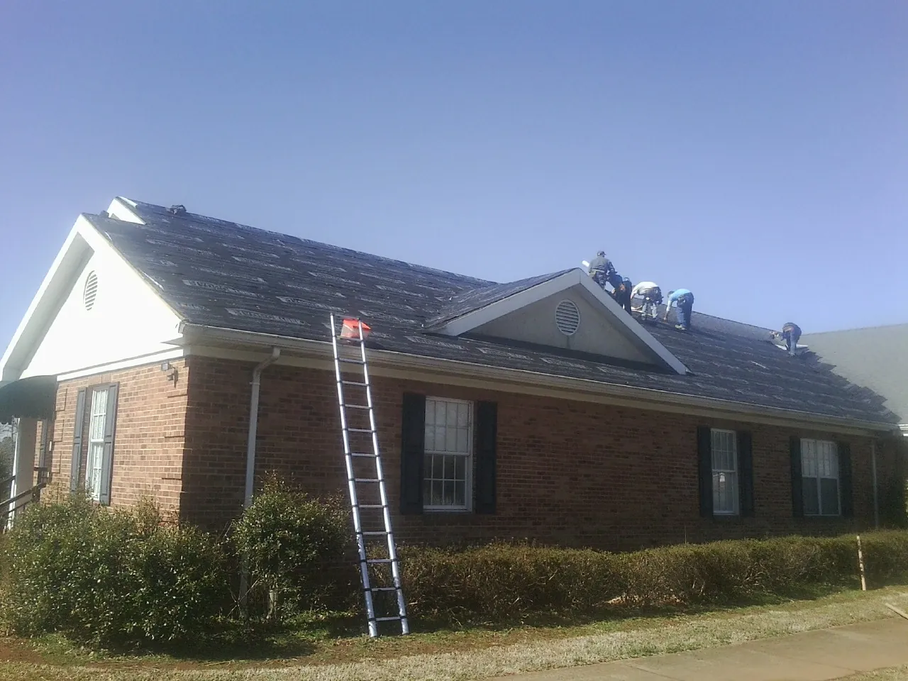 Crew tearing shingles off a brick ranch roof with a ladder set — Emergency Roof Repair work by our crew in Culver