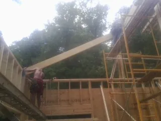 Carpenter raising a rafter beam on a new second story frame in Culver