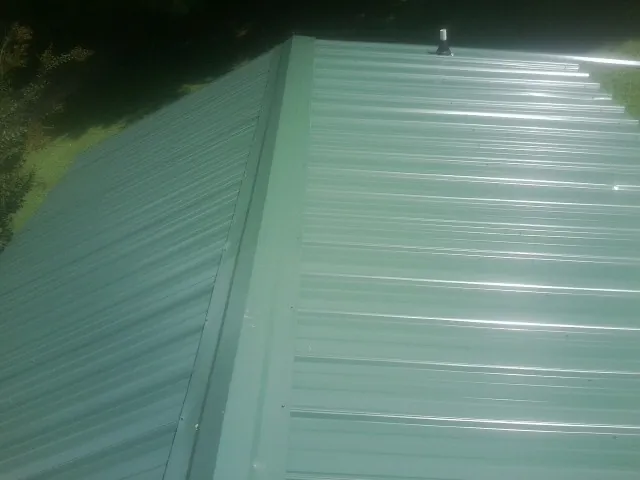 New green metal panels meeting at the ridge of a roof — Flat Roof Repair work by our crew in Culver
